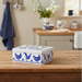 Decorative tin box with blue chicken design on a wooden surface in a kitchen setting.