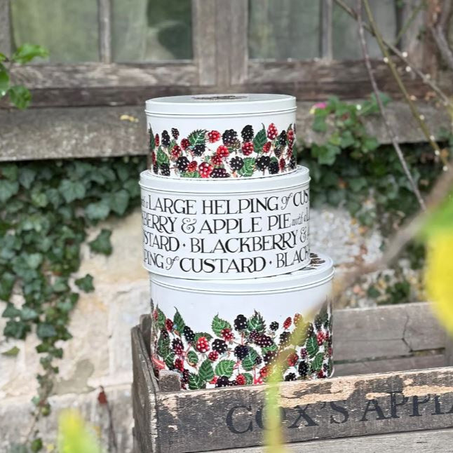 Stack of ceramic pots with blackberry design and text on a wooden surface outdoors.