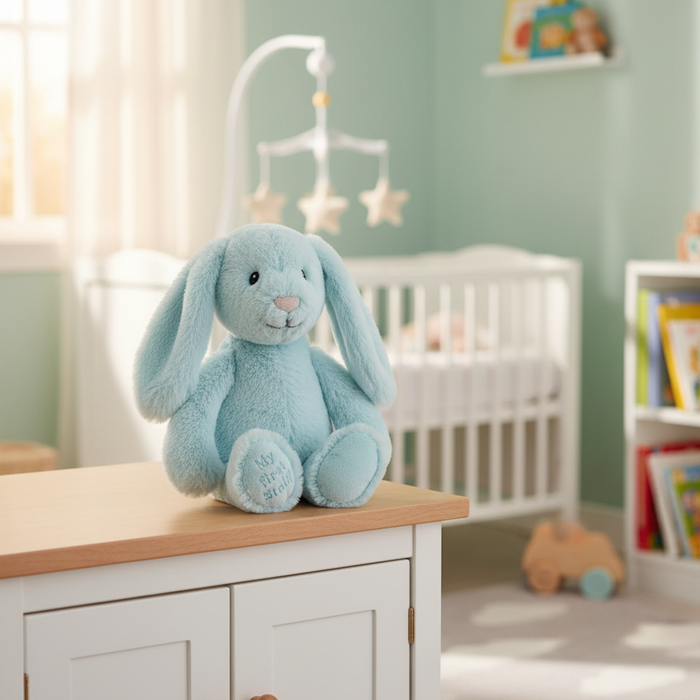 A light blue plush bunny toy sits on a white cabinet in a softly lit nursery with a crib, books, and pastel walls in the background.