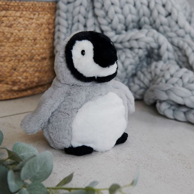The baby penguin sat on a carpet next to a grey knitted blanket 