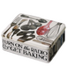 Tin box with kitchen utensil illustrations and text 'Turn on the Radio & Get Baking' on a white background