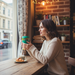 Woman sitting at a cafe table with a coffee cup and croissant, looking out the window.