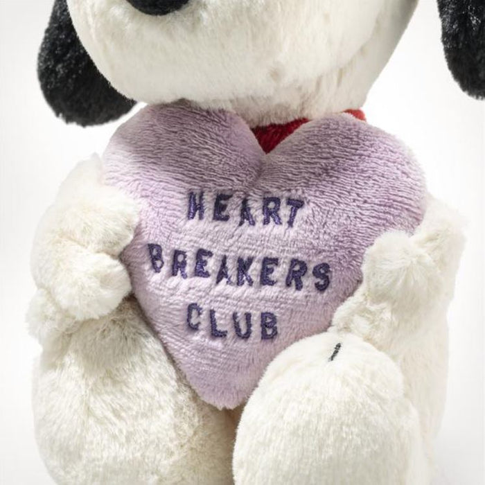 Stuffed dog holding a heart-shaped pillow with 'Heart Breakers Club' text on a white background