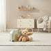 Teddy bear and suitcase in a child's room with toys on a shelf.