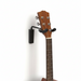 Guitar headstock attached to a wall-mounted guitar holder on a white background