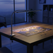 Desk with a lamp illuminating a puzzle on a wooden surface in a dimly lit room.