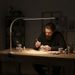 Man working on a craft project at a desk with a lamp illuminating his workspace.