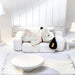 White plush dog toy sitting on a white couch in a minimalistic room.