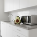 Avocado-shaped plush toy on a kitchen counter next to a microwave.
