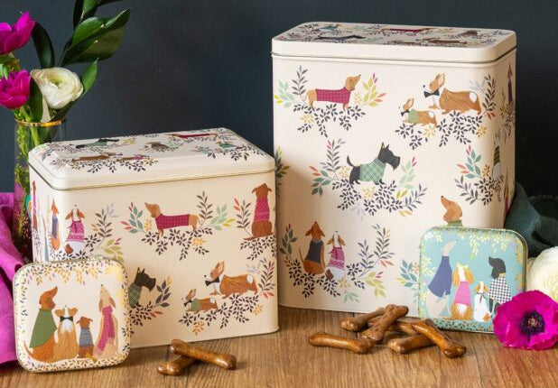 Decorative tins with animal illustrations on a wooden surface with flowers and treats.