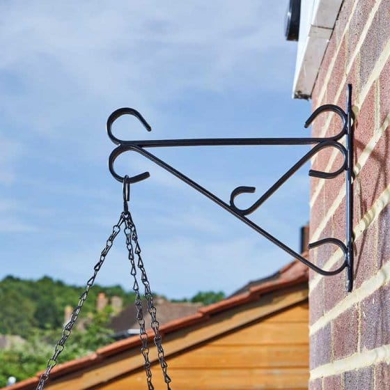 Black metal plant hanger attached to a brick wall with a clear blue sky in the background.