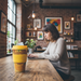 Woman working on a laptop with a yellow cup on a wooden table in a cozy cafe.