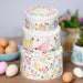 A off white stack of three cake tins with pastel coloured hens printed repeatedly around the tin with matching pastel coloured polka dots.