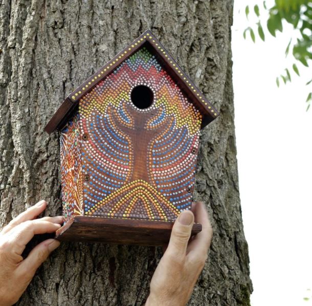 A bright multi-coloured painted dot mosaic bird house hanging up on a tree