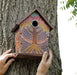 A bright multi-coloured painted dot mosaic bird house hanging up on a tree