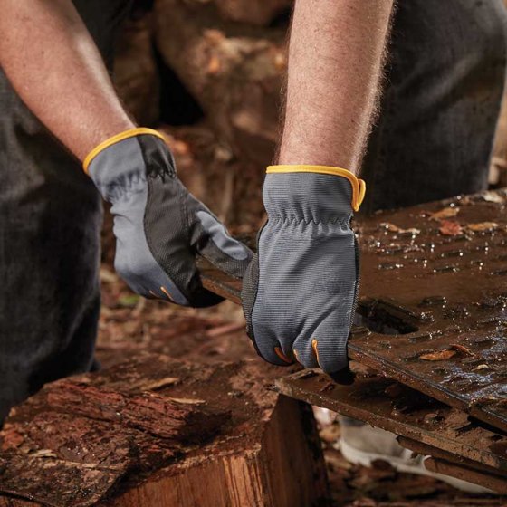 Black and grey gardening gloves with a yellow trim being used by a man moving wood in a forest 
