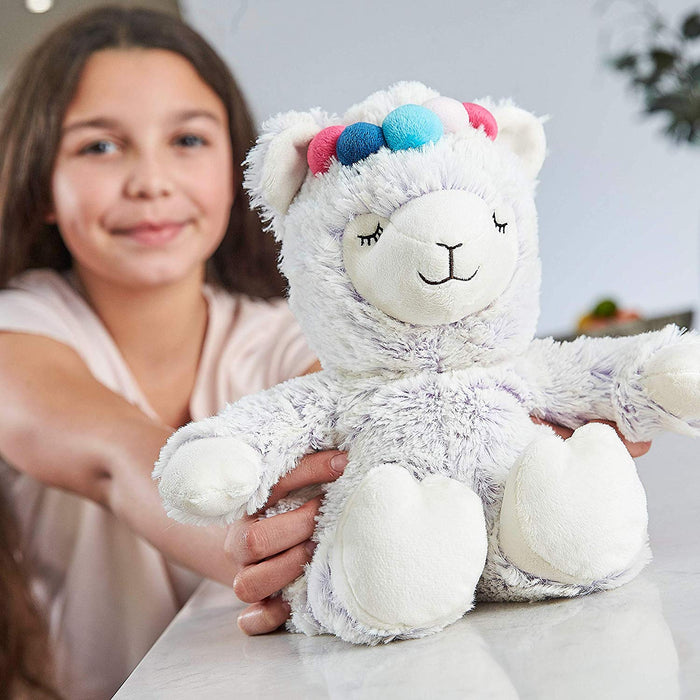 Young girl holding Warmies microwavable soft llama toy with multicoloured pom pom headband