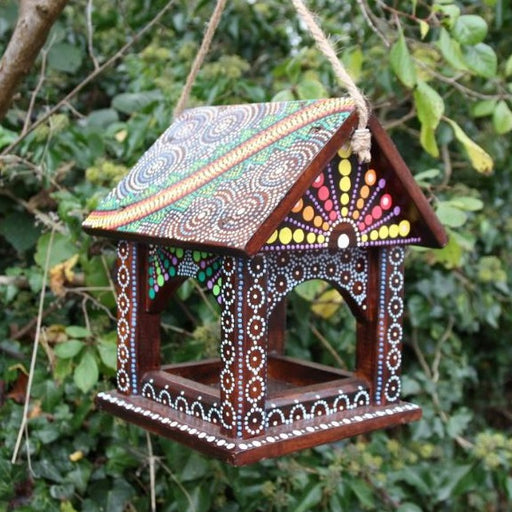 bird feeding table hung from a tree branch, the bird feeder is painted in various dot patterns in bright colours. 
