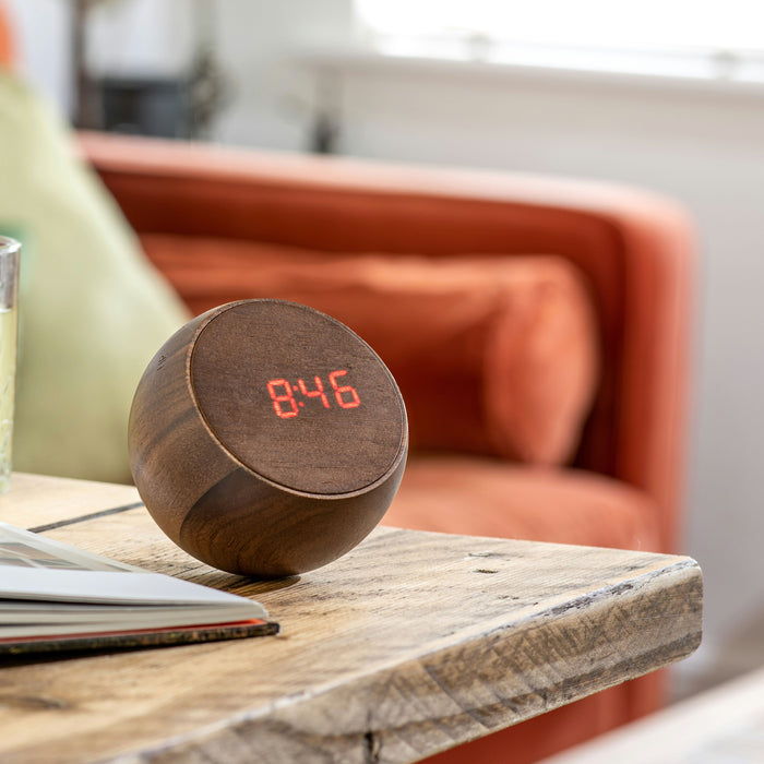 Gingko Tumbler LED Alarm Clock In Walnut Wood On A Wooden Table In A Living Room Setting