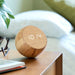 Gingko Design Tumbler Alarm Clock In Bamboo Showing The Time Sat On A Bedside Table