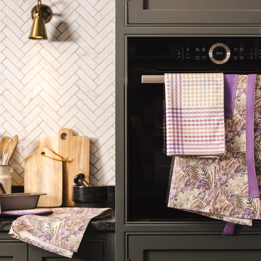 Ulster Weavers Purple Check tea Towel, Floral Heather Apron, & Check Oven Gloves In A Dark Grey Kitchen Setting
