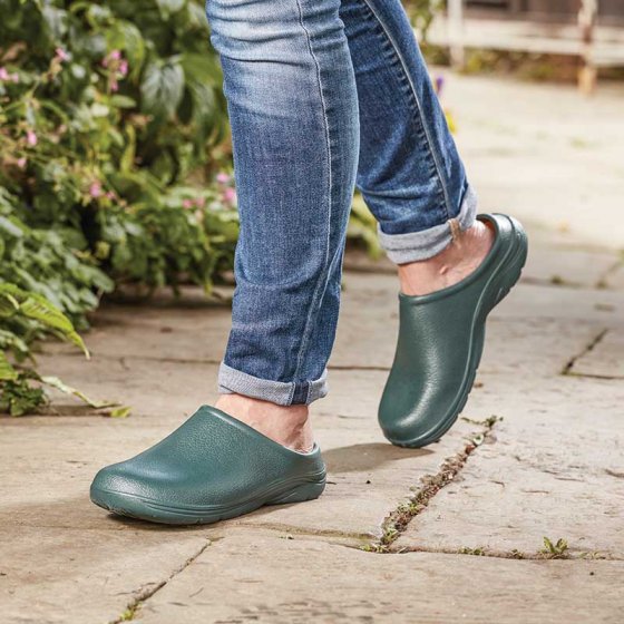 Bottle green clogs being used for walking down a garden path