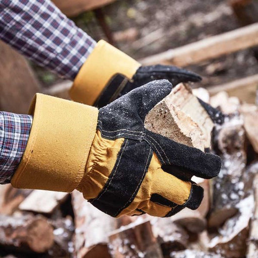 A pair of black and yellow work gloves being used by a man collecting chopped wood. 