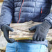 A pair of grey and black gardening gloves being used for carrying wooden logs.
