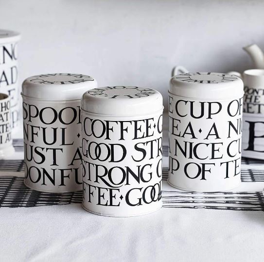 Set of three canisters that are cream with black writting repeated over them. They are displayed on a cream kitchen countertop. 