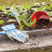 Children's blue gardening gloves next to a vegetable patch and a red bucket