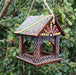 Dark wood bird feeder in a house style hanging from a tree branch. 