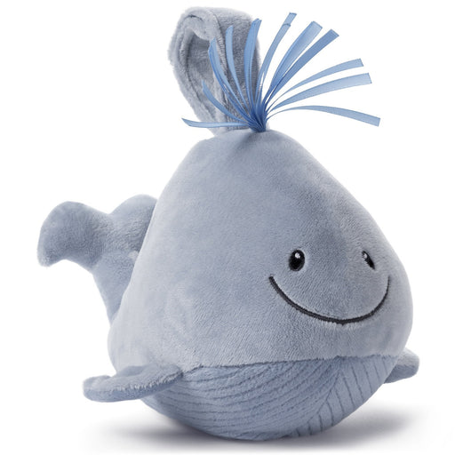 A light blue plush whale character with a happy smile and ribbon splashes from the head and a hoop for the toy to be attached to cribs, pushchairs and car seats. 