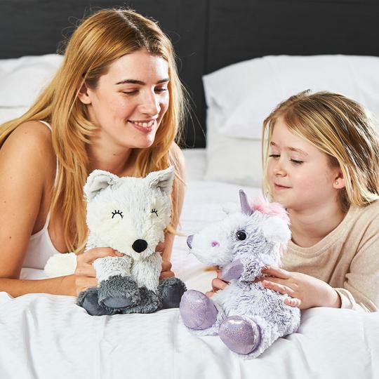 woman and young girl holding warmies purple sparkly unicorn and marshmallow fox heat up soft toy