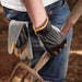 Black, grey and yellow gardening gloves being used my a man holding a gardening folk in a garden.